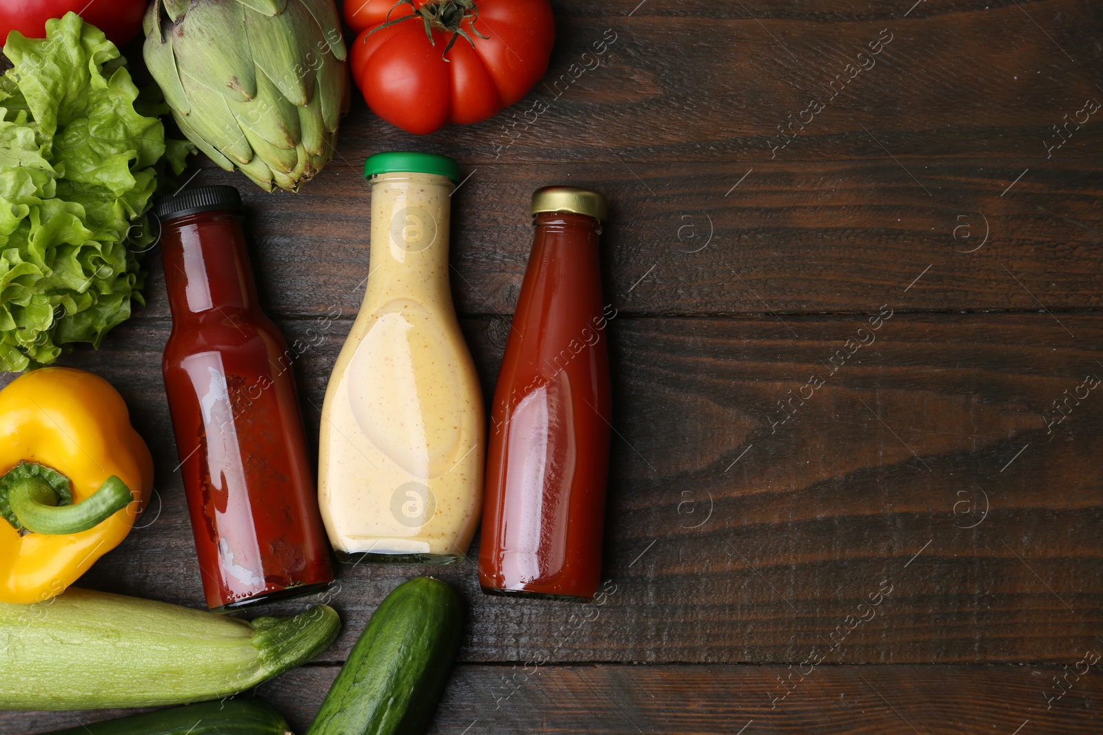 Photo of Tasty sauces in glass bottles and fresh products on wooden table, flat lay. Space for text