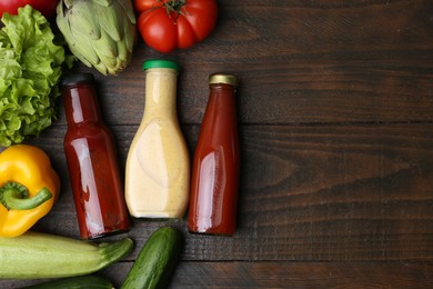 Photo of Tasty sauces in glass bottles and fresh products on wooden table, flat lay. Space for text