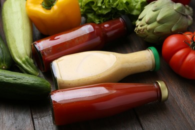 Photo of Tasty sauces in glass bottles and fresh products on wooden table, closeup