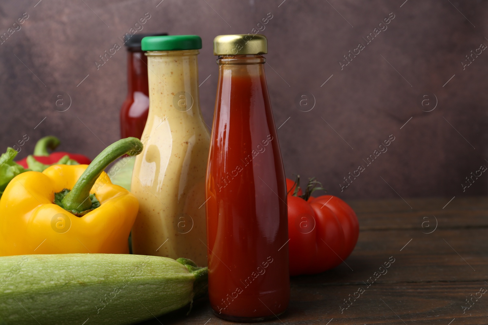 Photo of Tasty sauces in glass bottles and fresh products on wooden table, closeup. Space for text