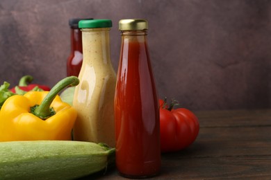 Photo of Tasty sauces in glass bottles and fresh products on wooden table, closeup. Space for text