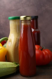 Photo of Tasty sauces in glass bottles and fresh products on wooden table, closeup