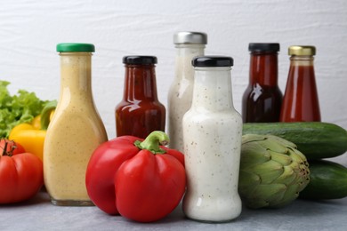 Photo of Tasty sauces in glass bottles and fresh products on light grey table, closeup