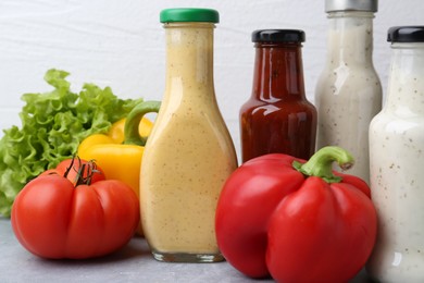 Photo of Tasty sauces in glass bottles and fresh products on light grey table, closeup