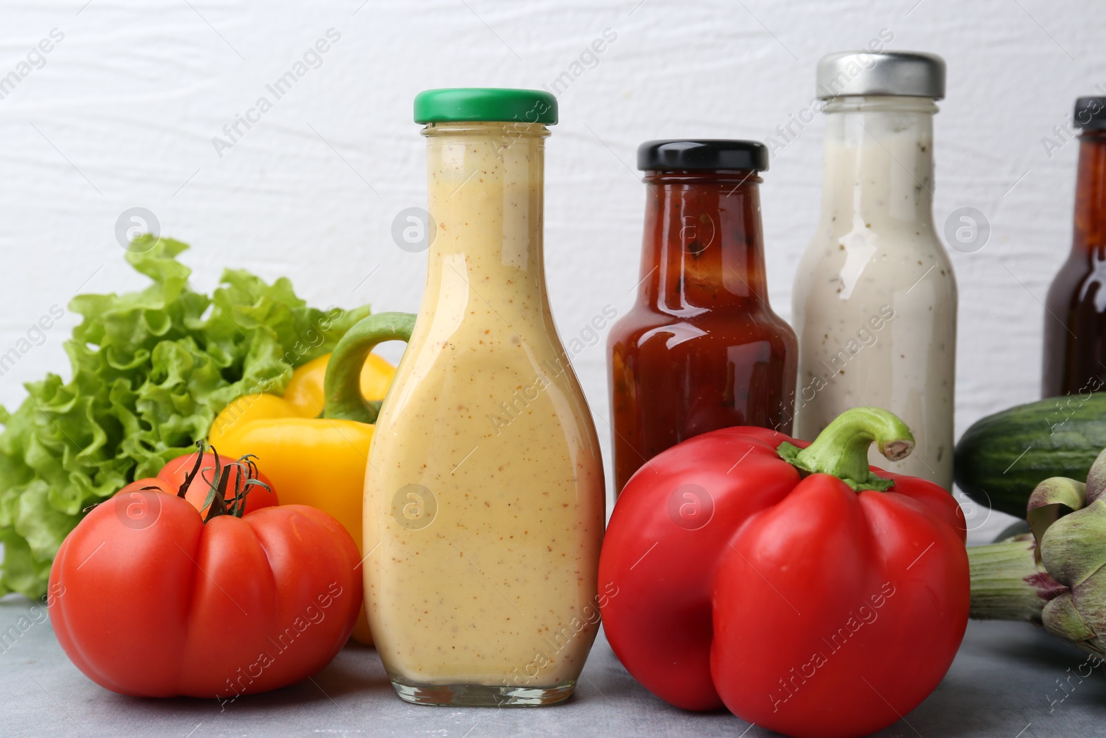 Photo of Tasty sauces in glass bottles and fresh products on light grey table, closeup