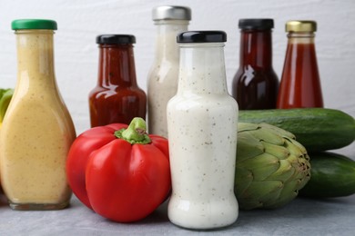 Photo of Tasty sauces in glass bottles and fresh products on light grey table, closeup