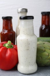 Photo of Tasty sauces in glass bottles and fresh products on light grey table, closeup