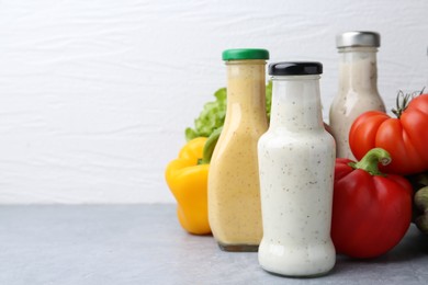 Photo of Tasty sauces in glass bottles and fresh products on light grey table, closeup. Space for text