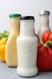 Photo of Tasty sauces in glass bottles and fresh products on light grey table, closeup