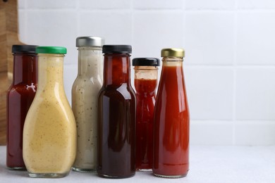 Photo of Tasty sauces in glass bottles on white table, closeup. Space for text