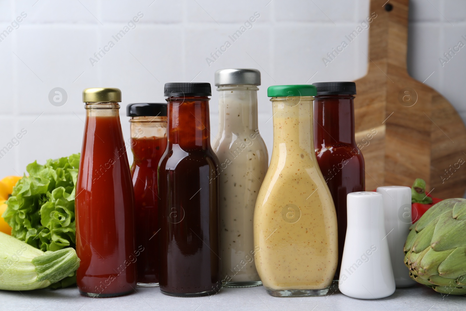 Photo of Tasty sauces in glass bottles and fresh products on white table, closeup