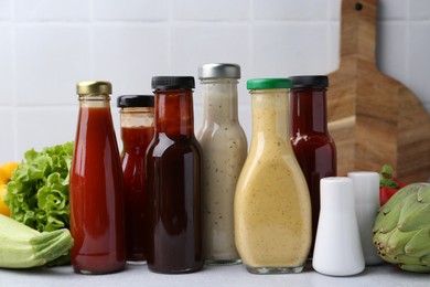 Photo of Tasty sauces in glass bottles and fresh products on white table, closeup