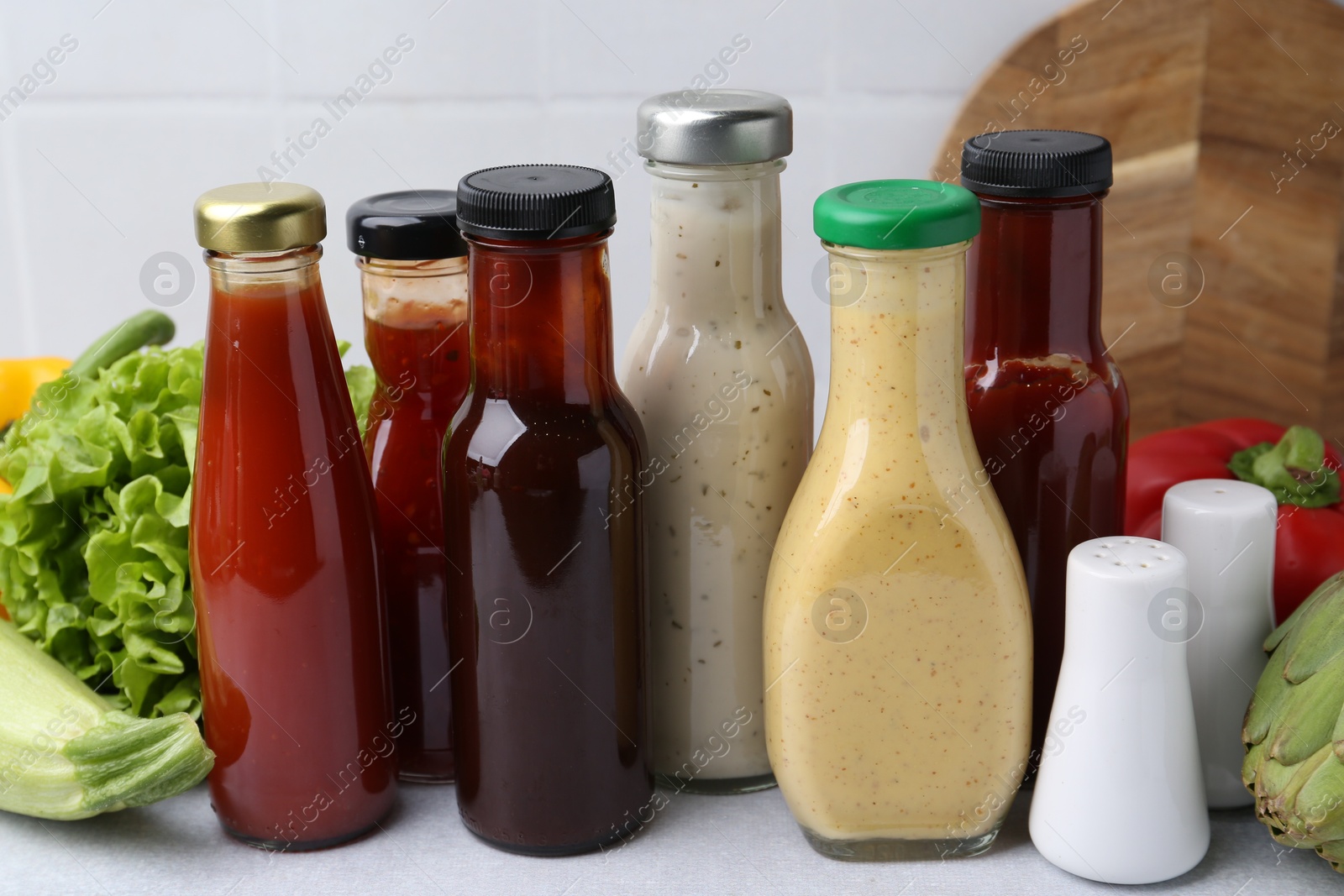 Photo of Tasty sauces in glass bottles and fresh products on white table, closeup