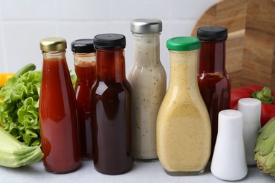 Photo of Tasty sauces in glass bottles and fresh products on white table, closeup