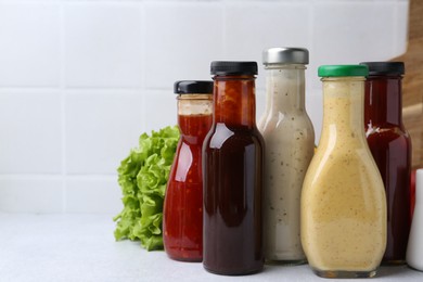 Photo of Tasty sauces in glass bottles on white table, closeup. Space for text