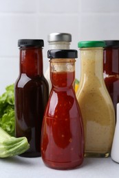 Photo of Tasty sauces in glass bottles and fresh products on white table, closeup