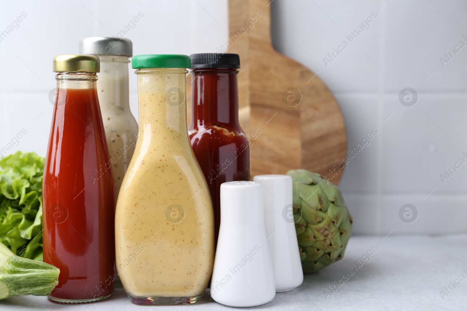 Photo of Tasty sauces in glass bottles and fresh products on white table, closeup. Space for text