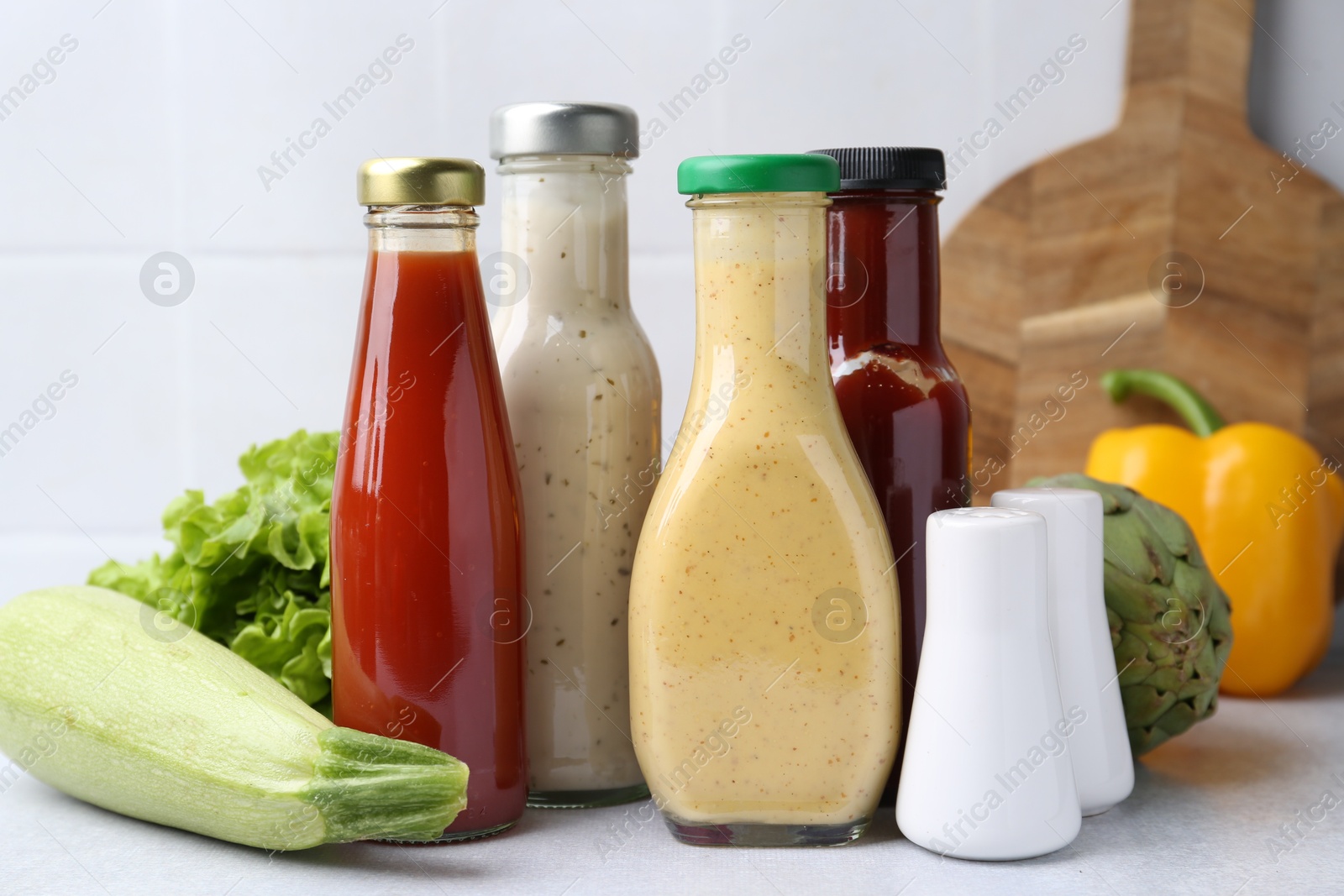 Photo of Tasty sauces in glass bottles and fresh products on white table, closeup