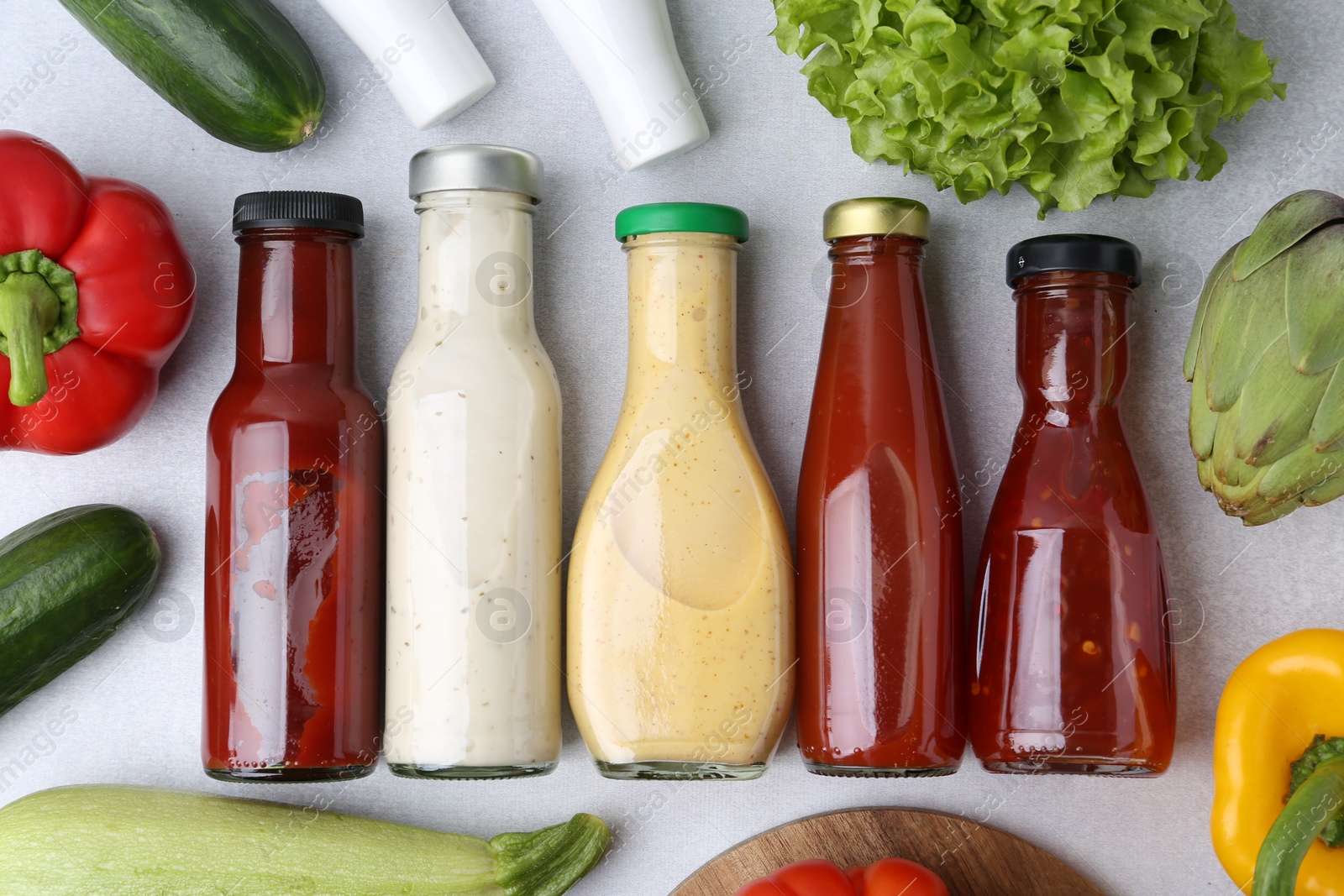 Photo of Tasty sauces in glass bottles and fresh products on white table, flat lay