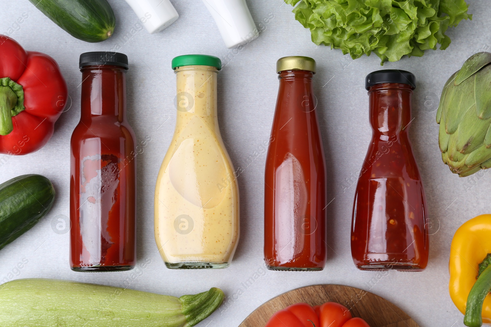 Photo of Tasty sauces in glass bottles and fresh products on white table, flat lay