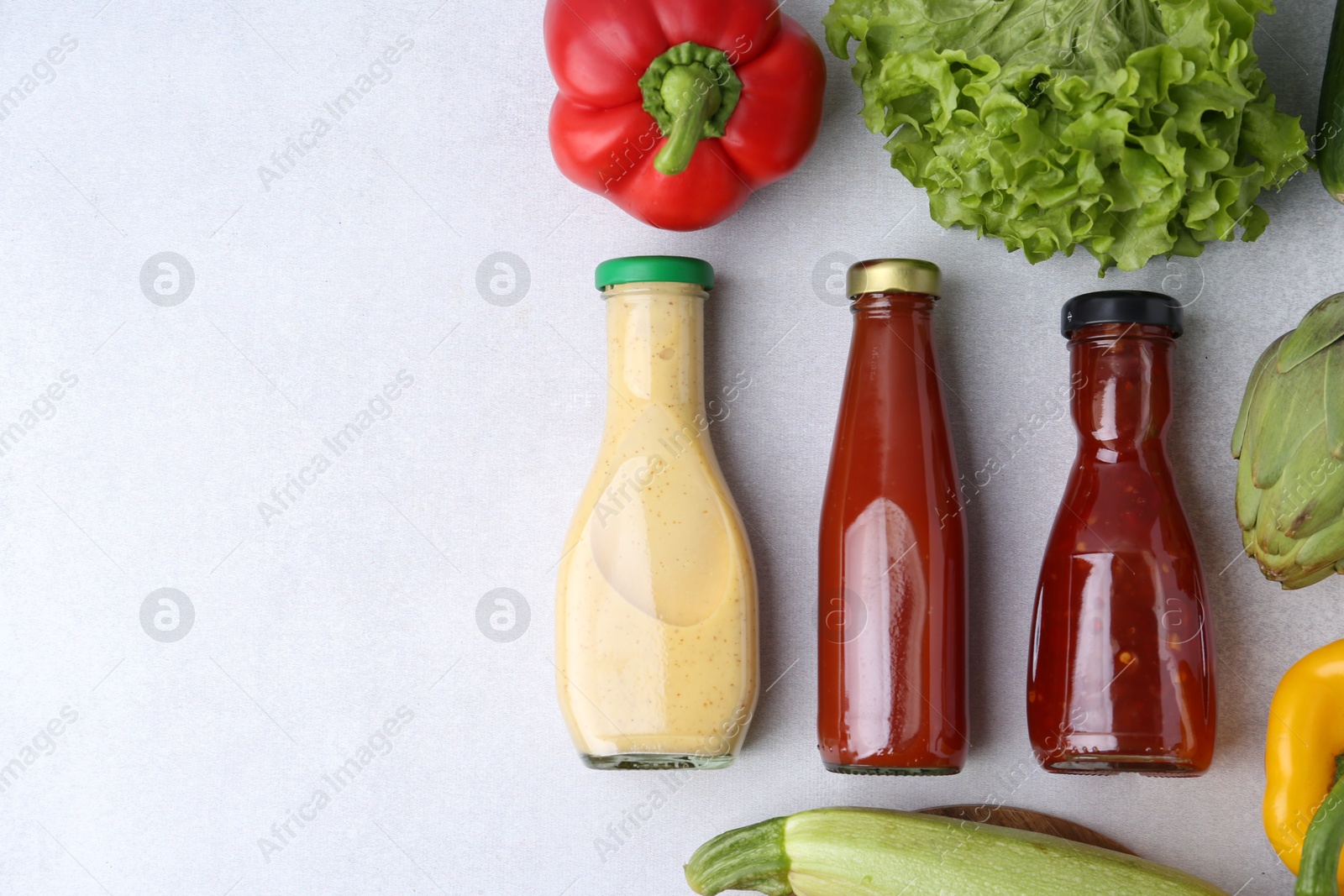 Photo of Tasty sauces in glass bottles and fresh products on white table, flat lay. Space for text