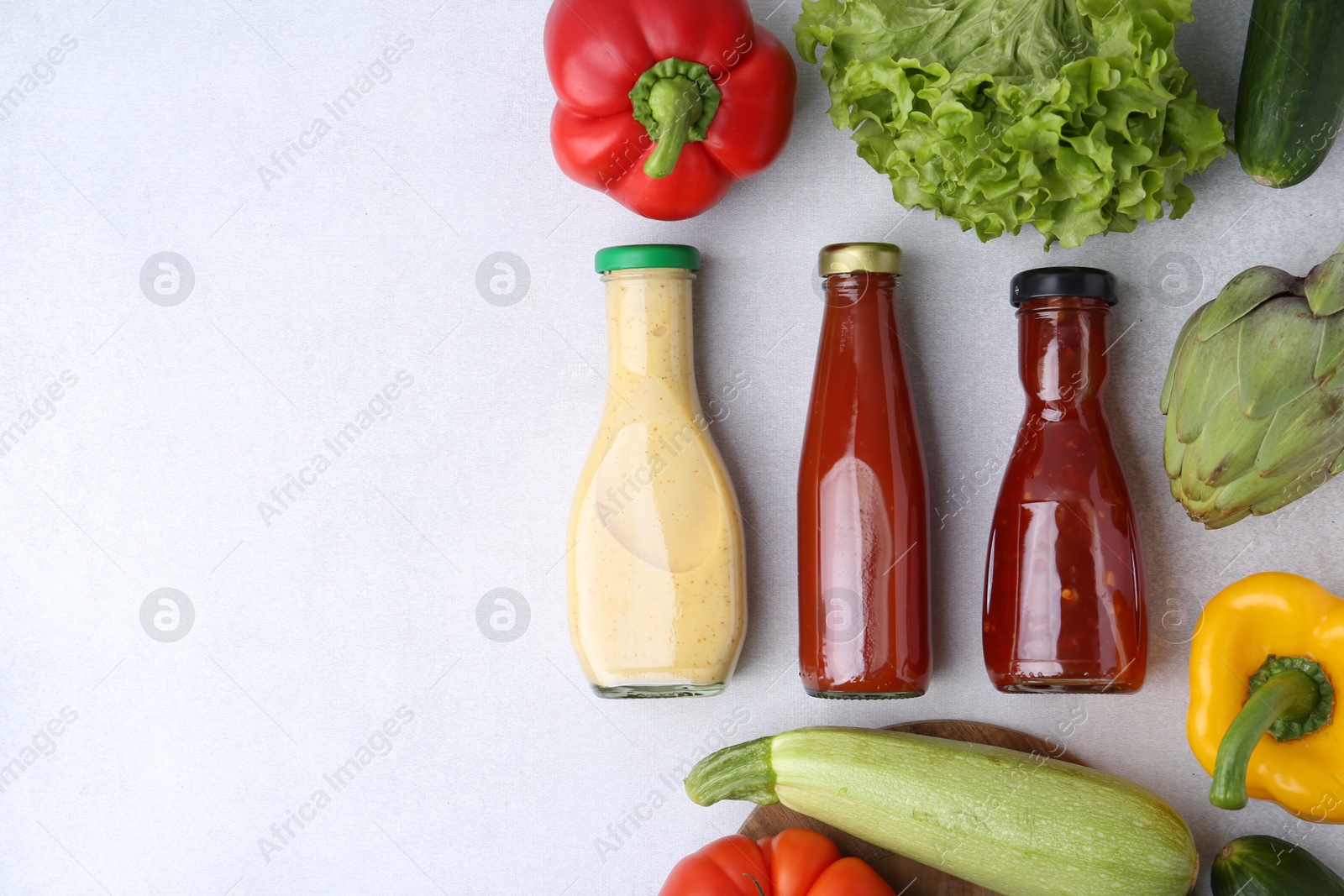 Photo of Tasty sauces in glass bottles and fresh products on white table, flat lay. Space for text