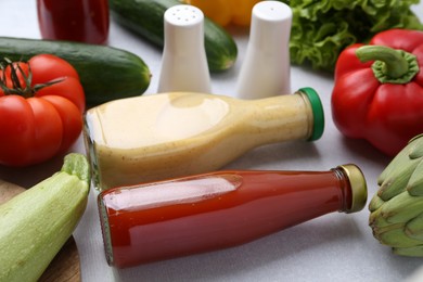 Photo of Tasty sauces in glass bottles and fresh products on white table, closeup