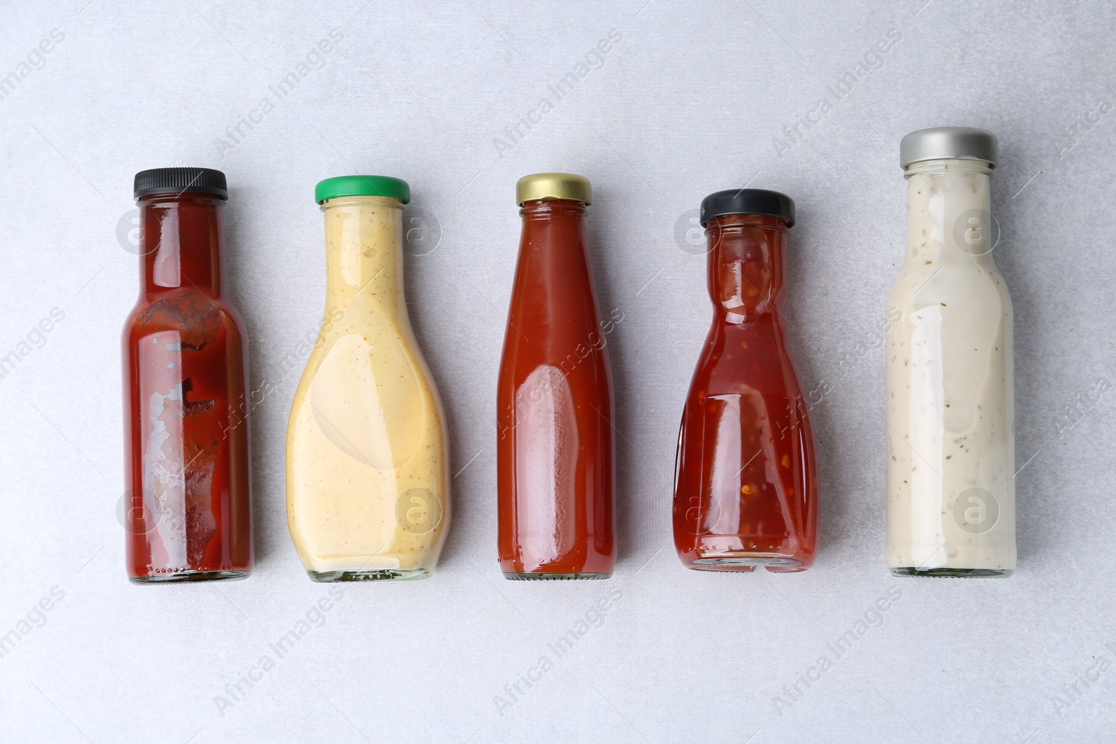 Photo of Tasty sauces in glass bottles on white table, flat lay