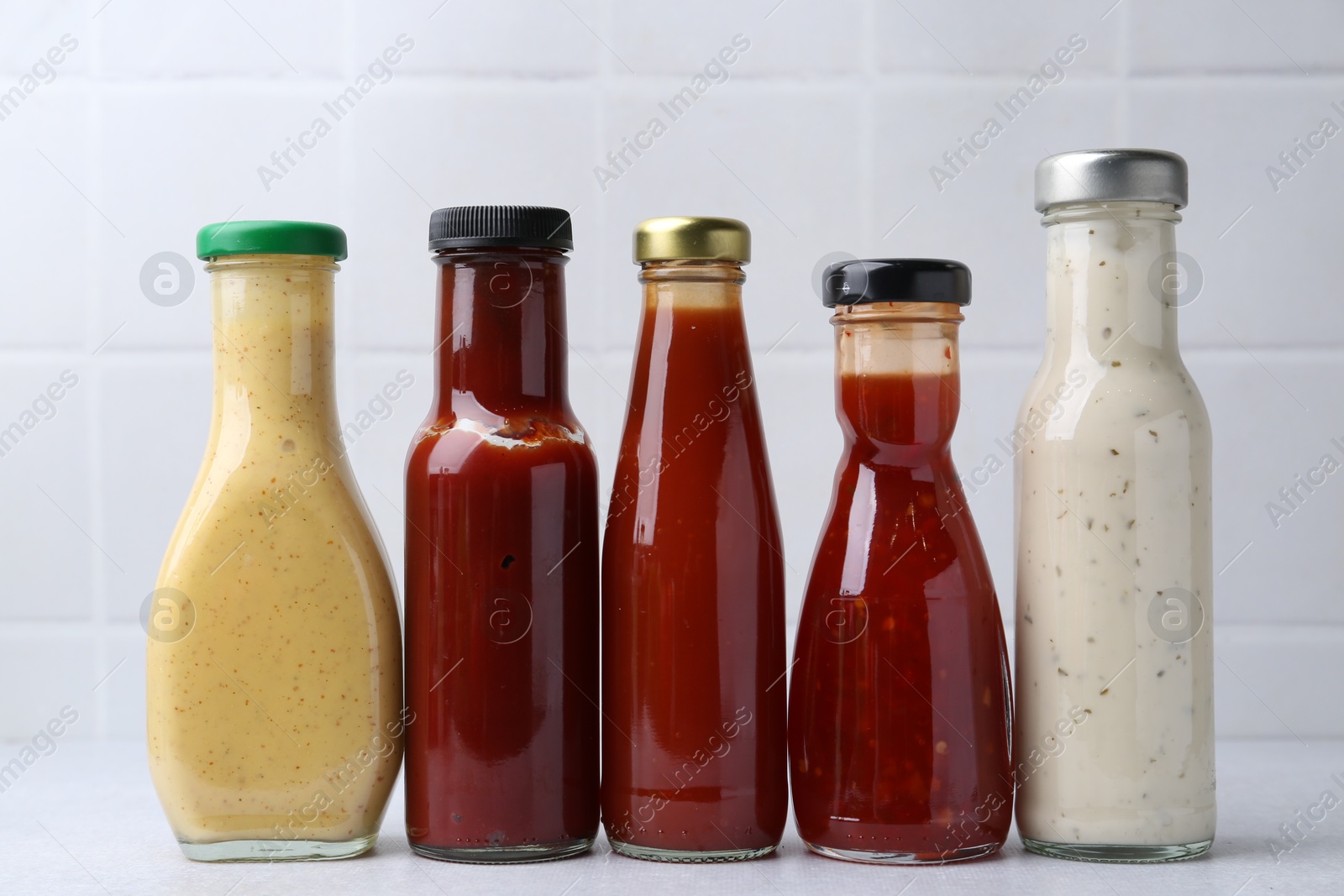 Photo of Tasty sauces in glass bottles on white table, closeup