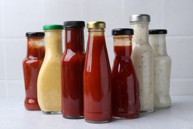 Photo of Tasty sauces in glass bottles on white table, closeup