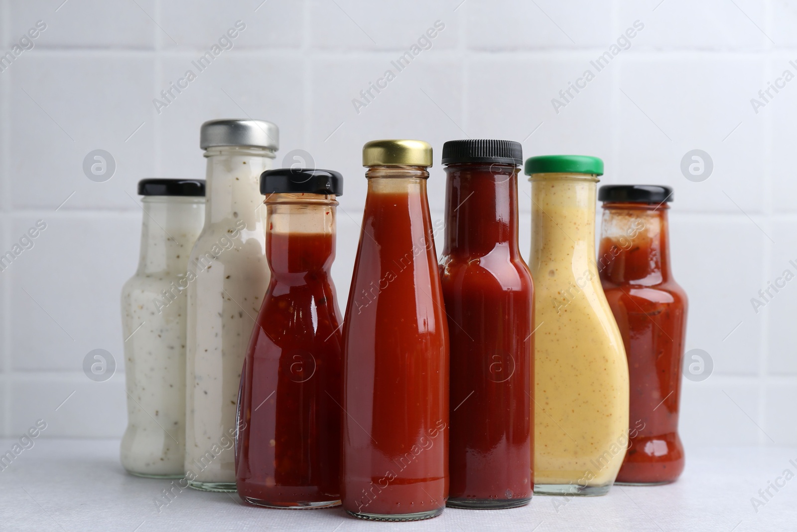 Photo of Tasty sauces in glass bottles on white table, closeup