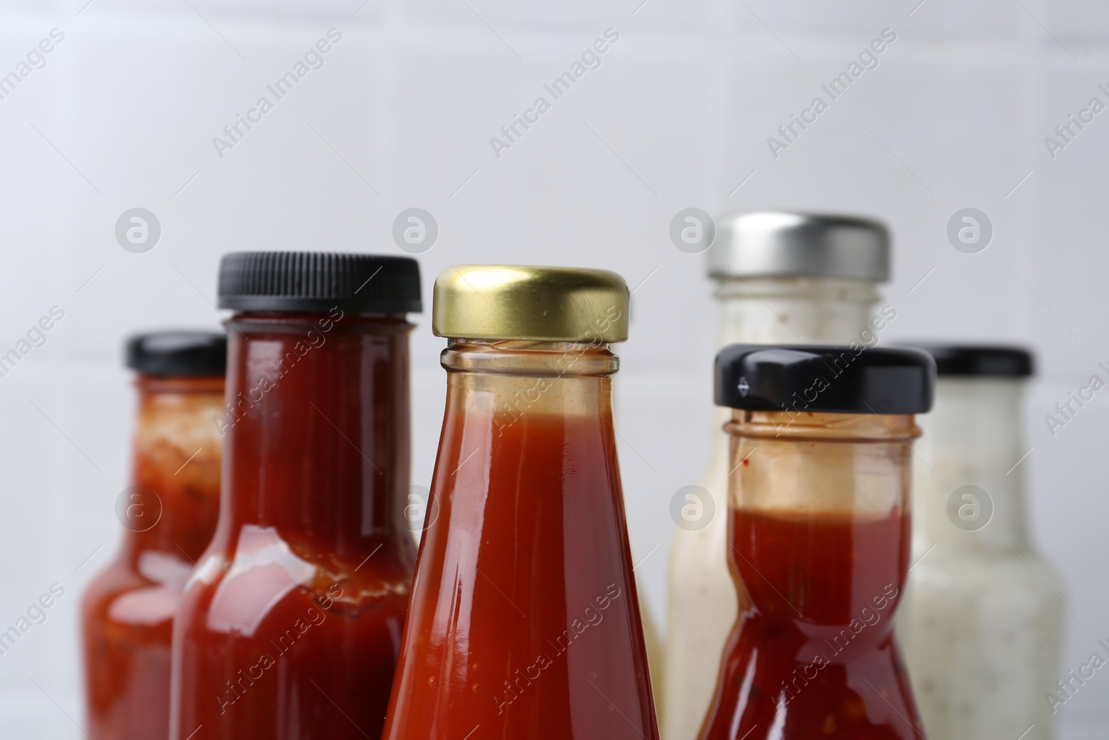 Photo of Tasty sauces in glass bottles on white background, closeup