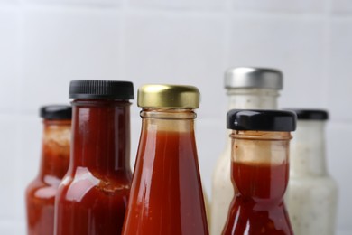 Photo of Tasty sauces in glass bottles on white background, closeup