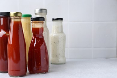 Photo of Tasty sauces in glass bottles on white table, closeup. Space for text