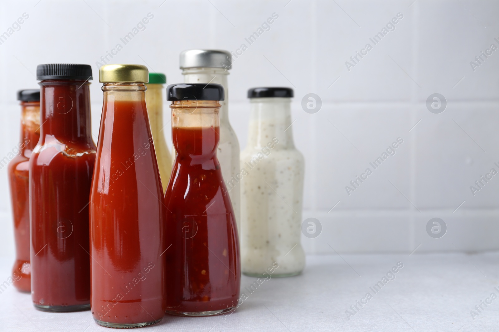 Photo of Tasty sauces in glass bottles on white table, closeup. Space for text