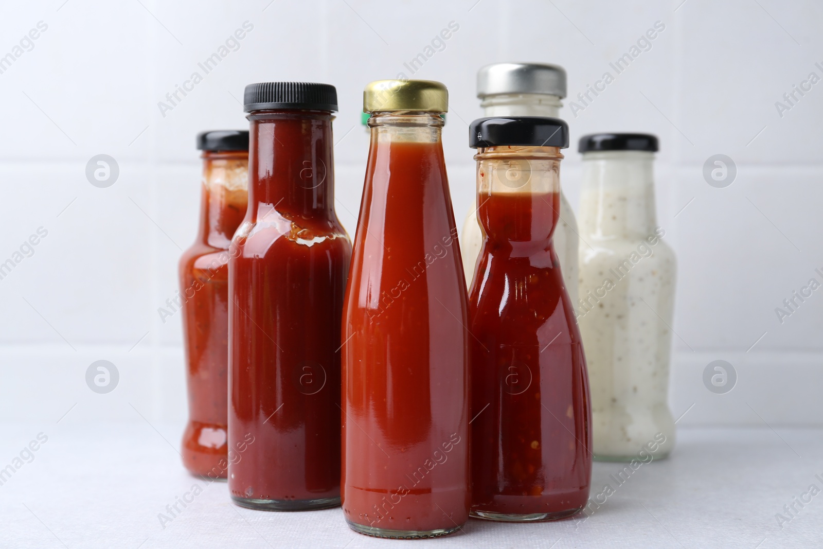 Photo of Tasty sauces in glass bottles on white table, closeup