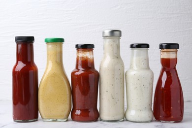 Photo of Tasty sauces in glass bottles on white table, closeup