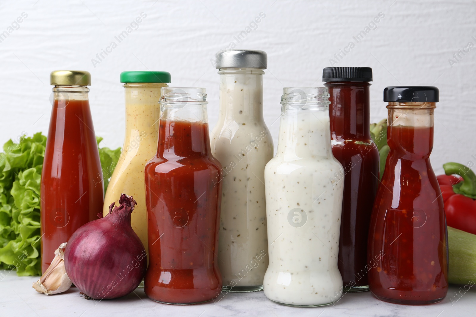 Photo of Tasty sauces in glass bottles and fresh products on white marble table, closeup