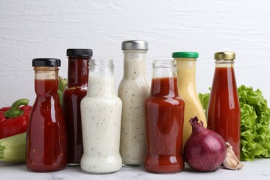 Photo of Tasty sauces in glass bottles and fresh products on white marble table, closeup