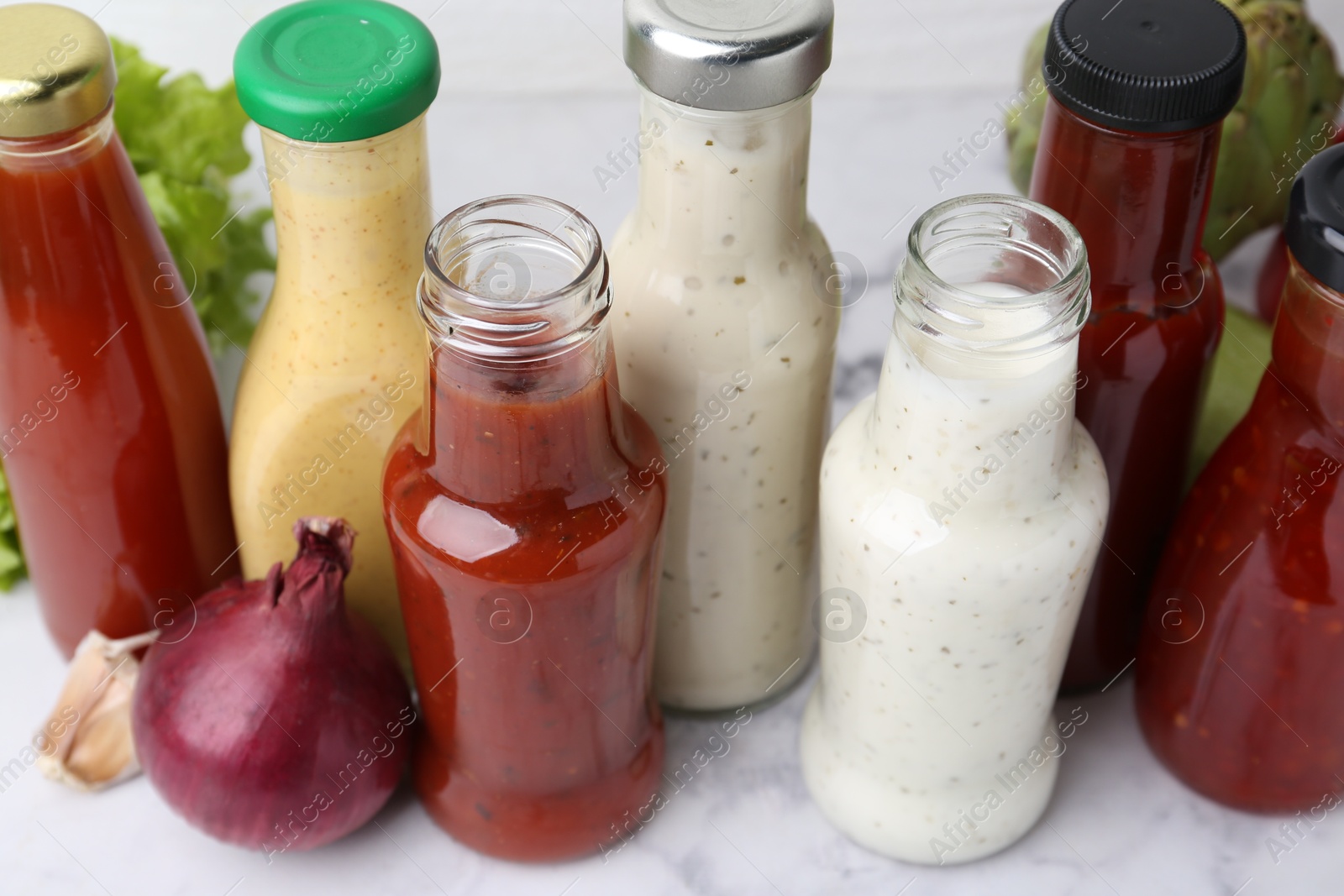 Photo of Tasty sauces in glass bottles and fresh products on white marble table, closeup