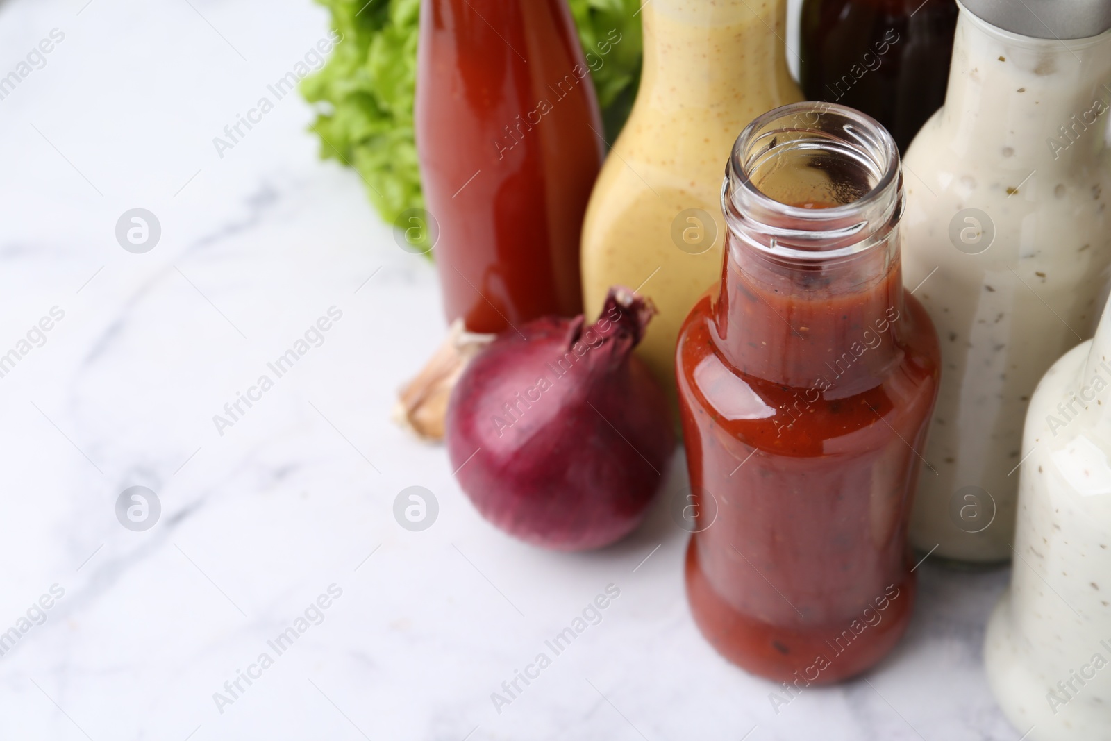 Photo of Tasty sauces in glass bottles on white marble table, closeup. Space for text