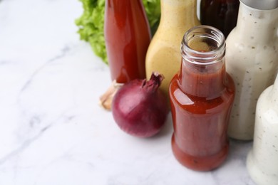 Photo of Tasty sauces in glass bottles on white marble table, closeup. Space for text