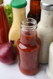 Photo of Tasty sauces in glass bottles on white marble table, closeup