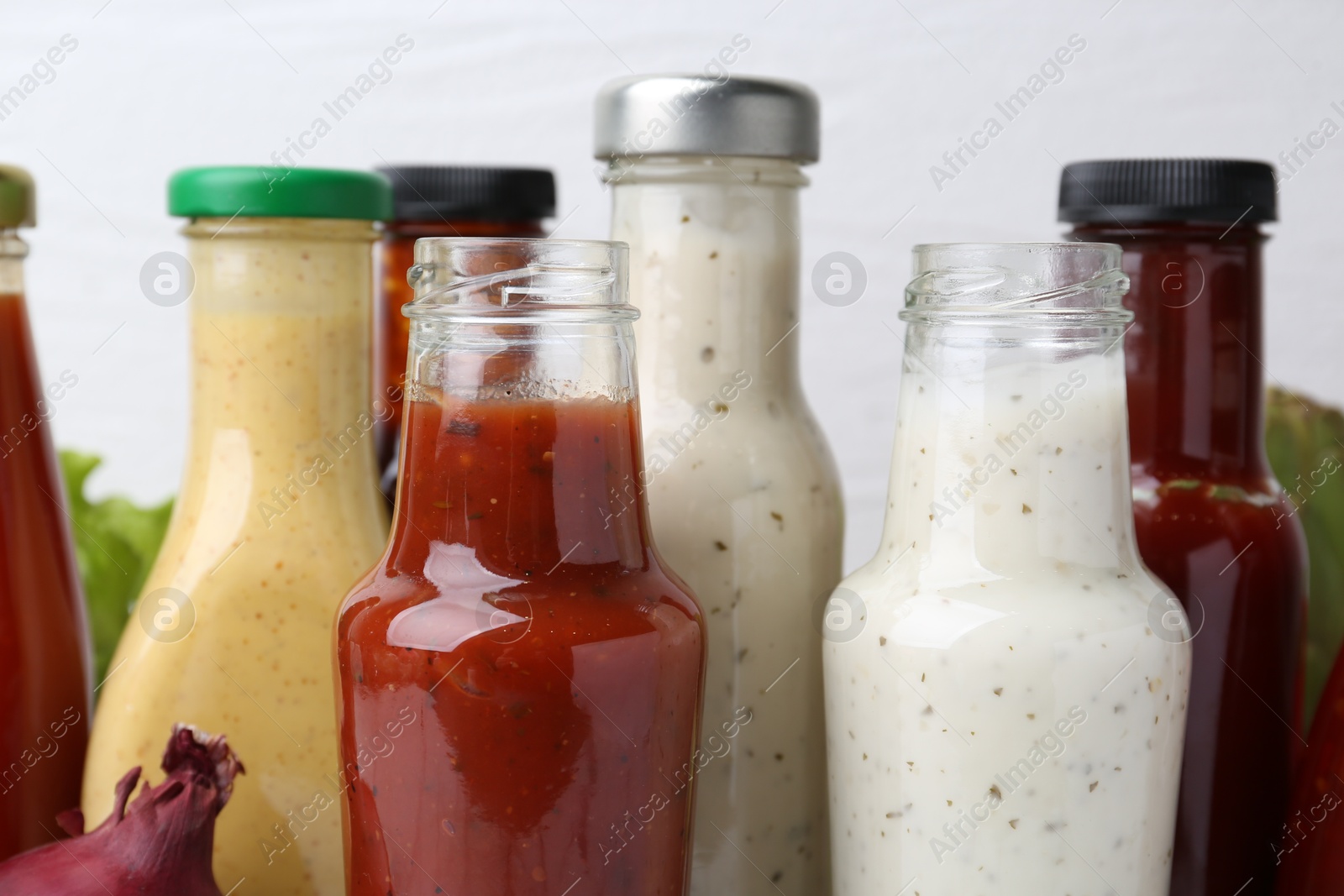 Photo of Tasty sauces in glass bottles on white background, closeup