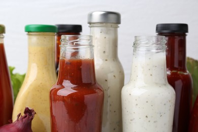 Tasty sauces in glass bottles on white background, closeup