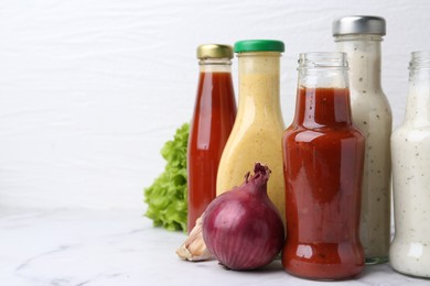 Photo of Tasty sauces in glass bottles on white marble table, closeup. Space for text