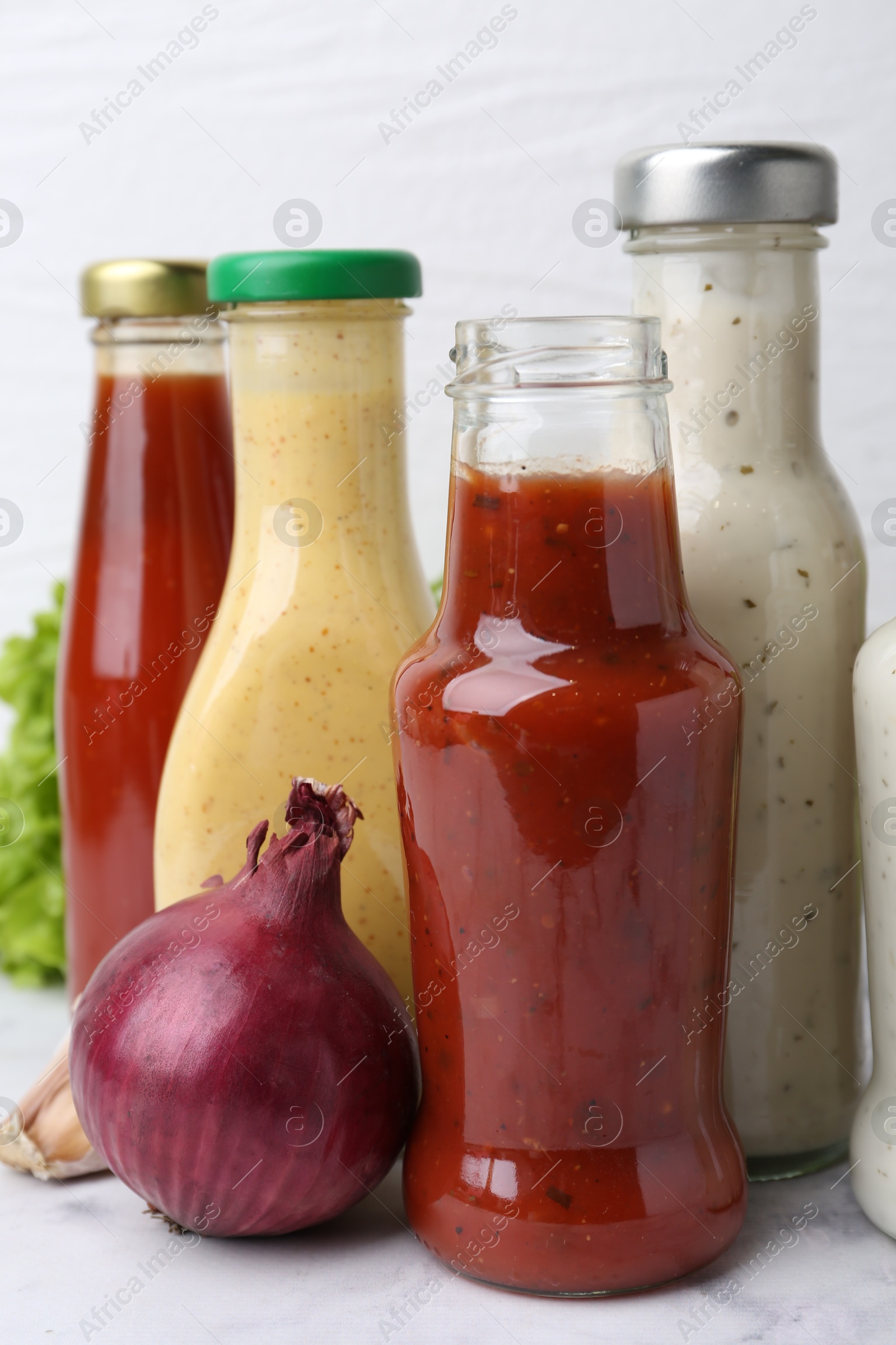 Photo of Tasty sauces in glass bottles and fresh products on white marble table, closeup