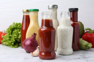 Photo of Tasty sauces in glass bottles and fresh products on white marble table, closeup