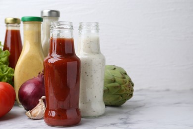 Tasty sauces in glass bottles and fresh products on white marble table, closeup. Space for text