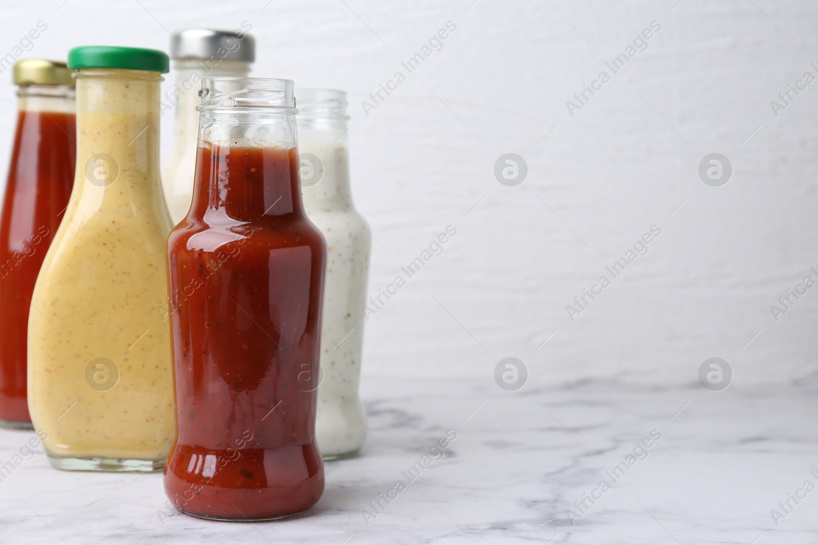 Photo of Tasty sauces in glass bottles on white marble table, closeup. Space for text